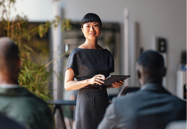 Woman speaking to a group with clipboard.