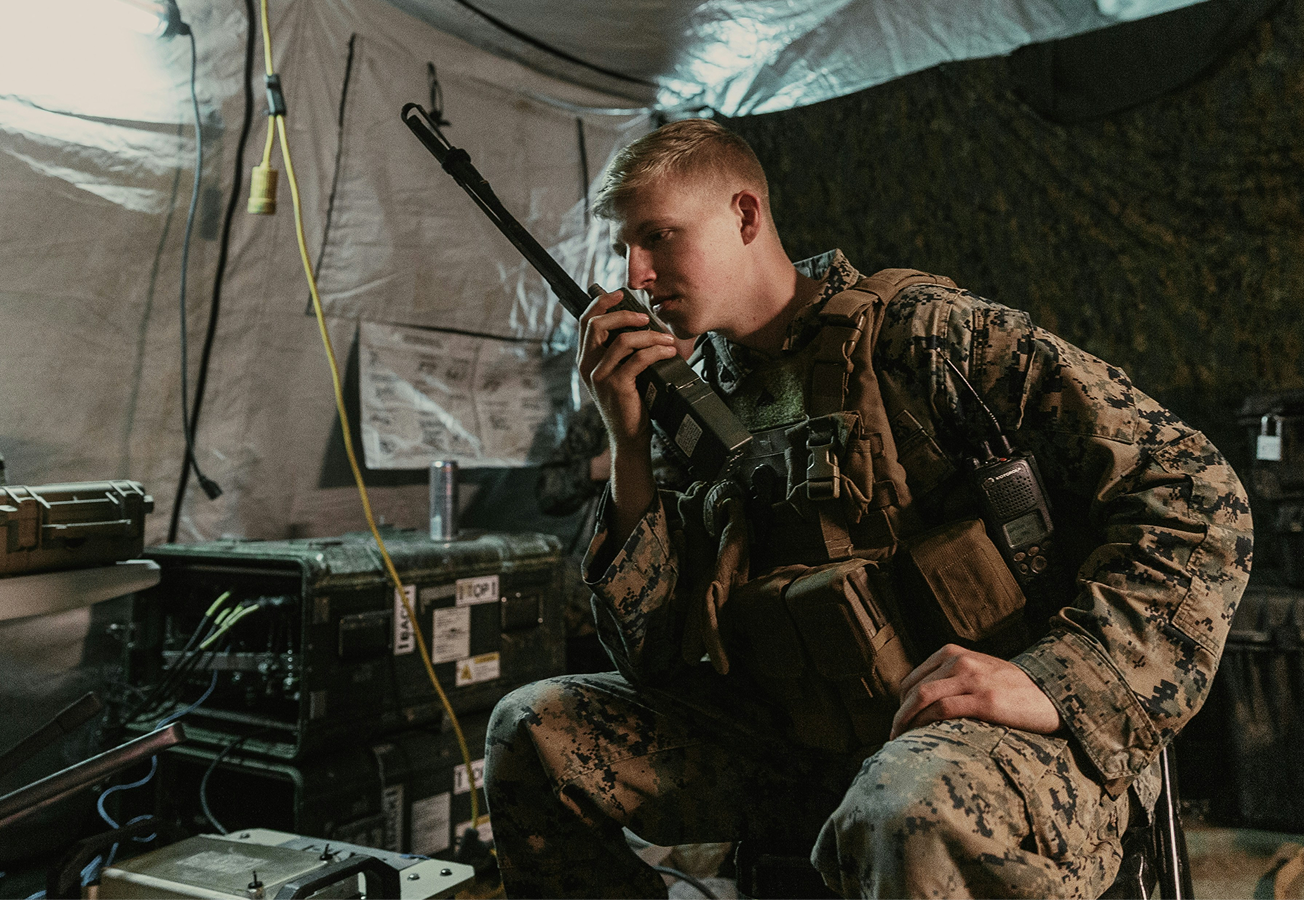 Military soldier in an operations tent speaking on a radio.