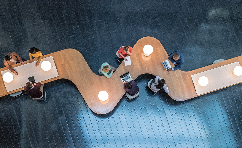 Long table with office workers taking and using laptops.